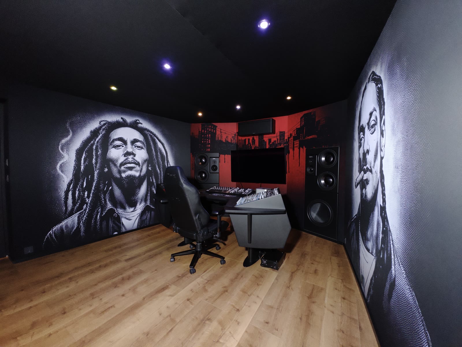 Wide view of the full control room in daylight: portrait murals on both side walls, the red skyline artwork behind the monitor wall, workstation in the center.