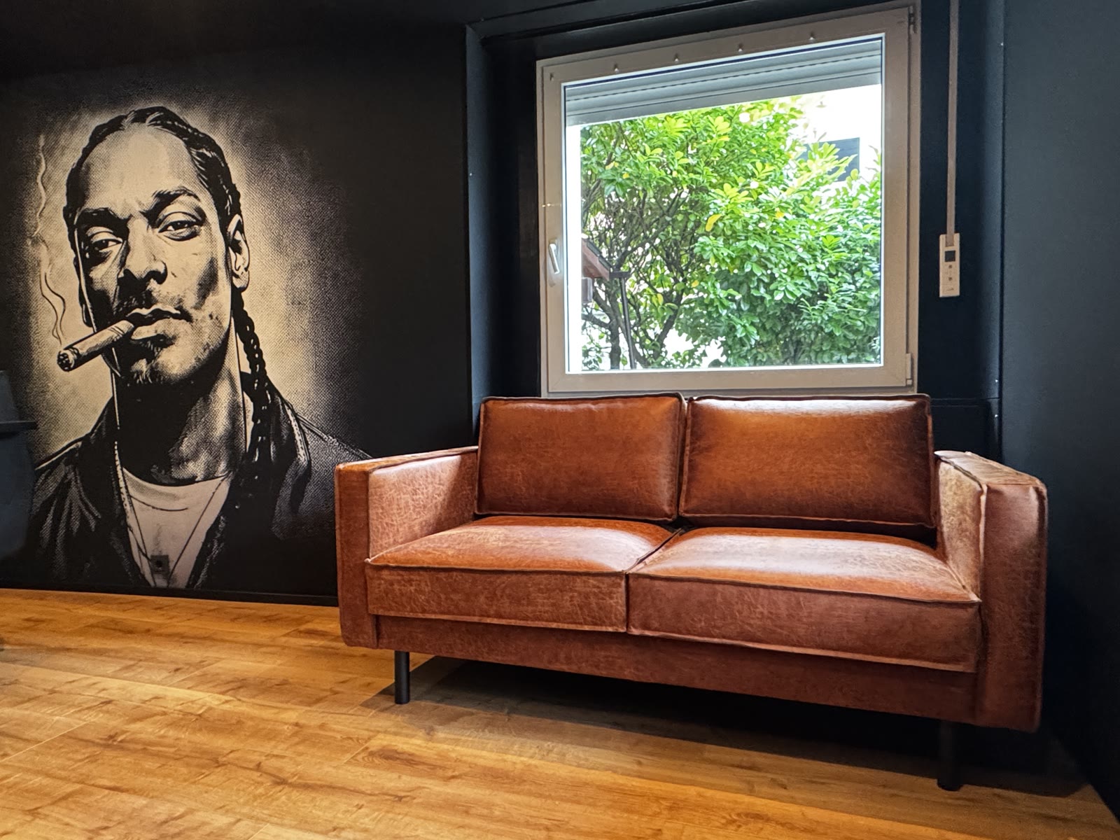 Cognac leather sofa beneath the window, framed by the large-format portrait mural on the lounge wall.