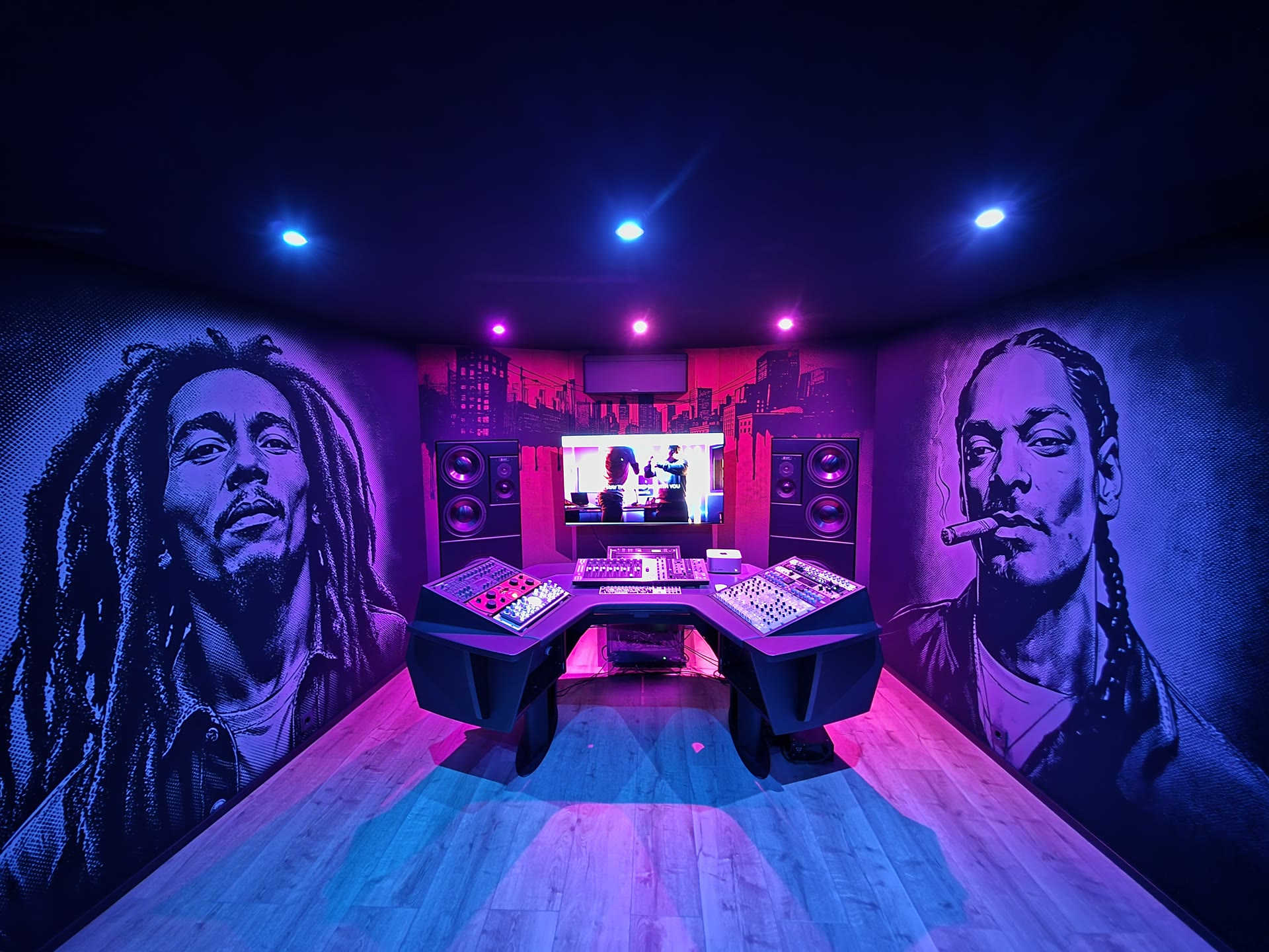 The MMA Studios main control room at night: flush-mounted main monitor stacks left and right of the screen, the central workstation with analog racks, large-format portrait murals on acoustically transparent fabric, lit in deep magenta and blue.