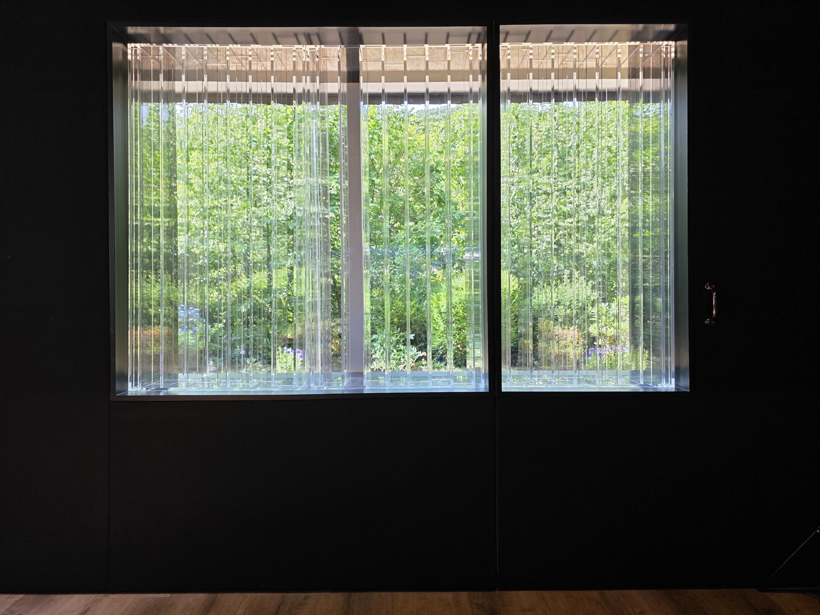 The Lightffusor by day: transparent acrylic diffuser slats in front of the rear-wall windows, with an unobstructed green view into the garden.