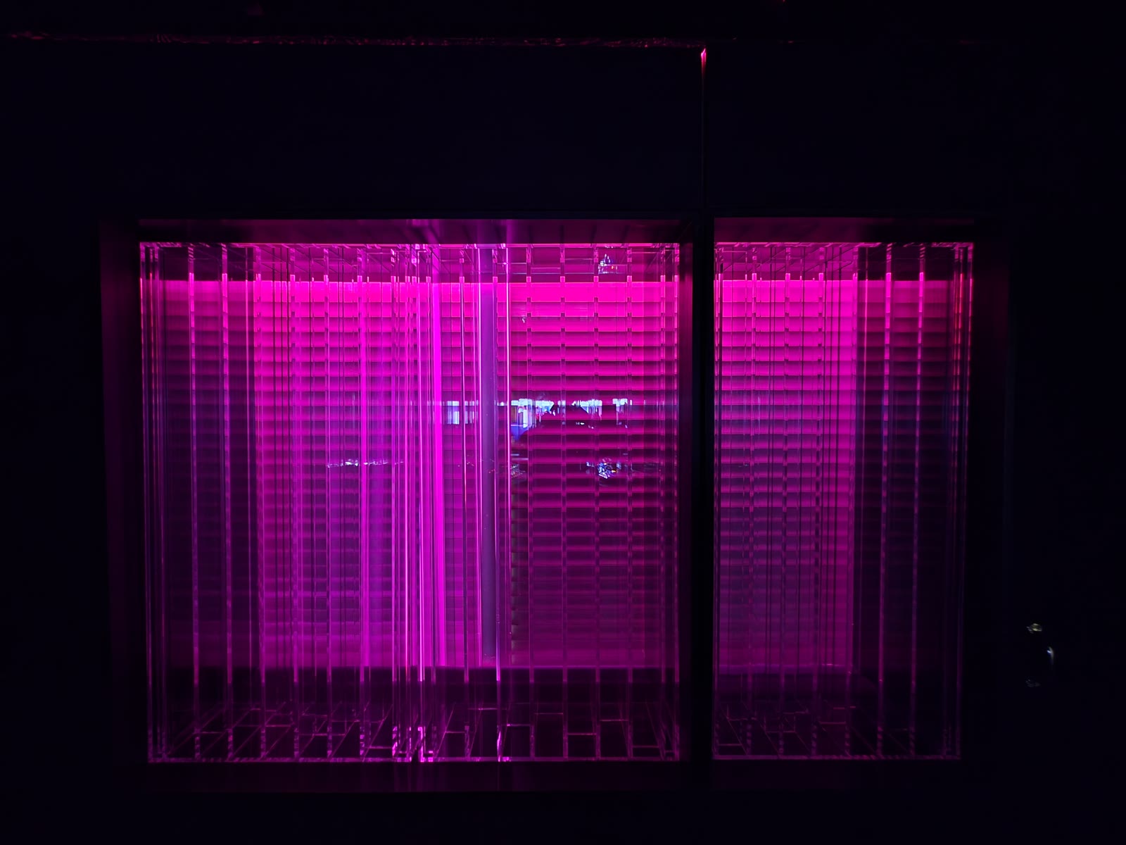 The Lightffusor at night: the transparent rear-wall diffuser glowing in deep magenta, its slat structure acting as acoustic diffusion.